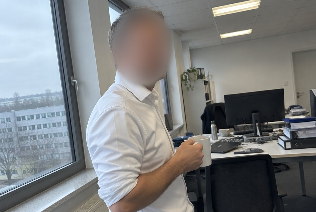 Daniel mit Kaffeetasse in seinem Büro, Gesicht unkenntlich gemacht